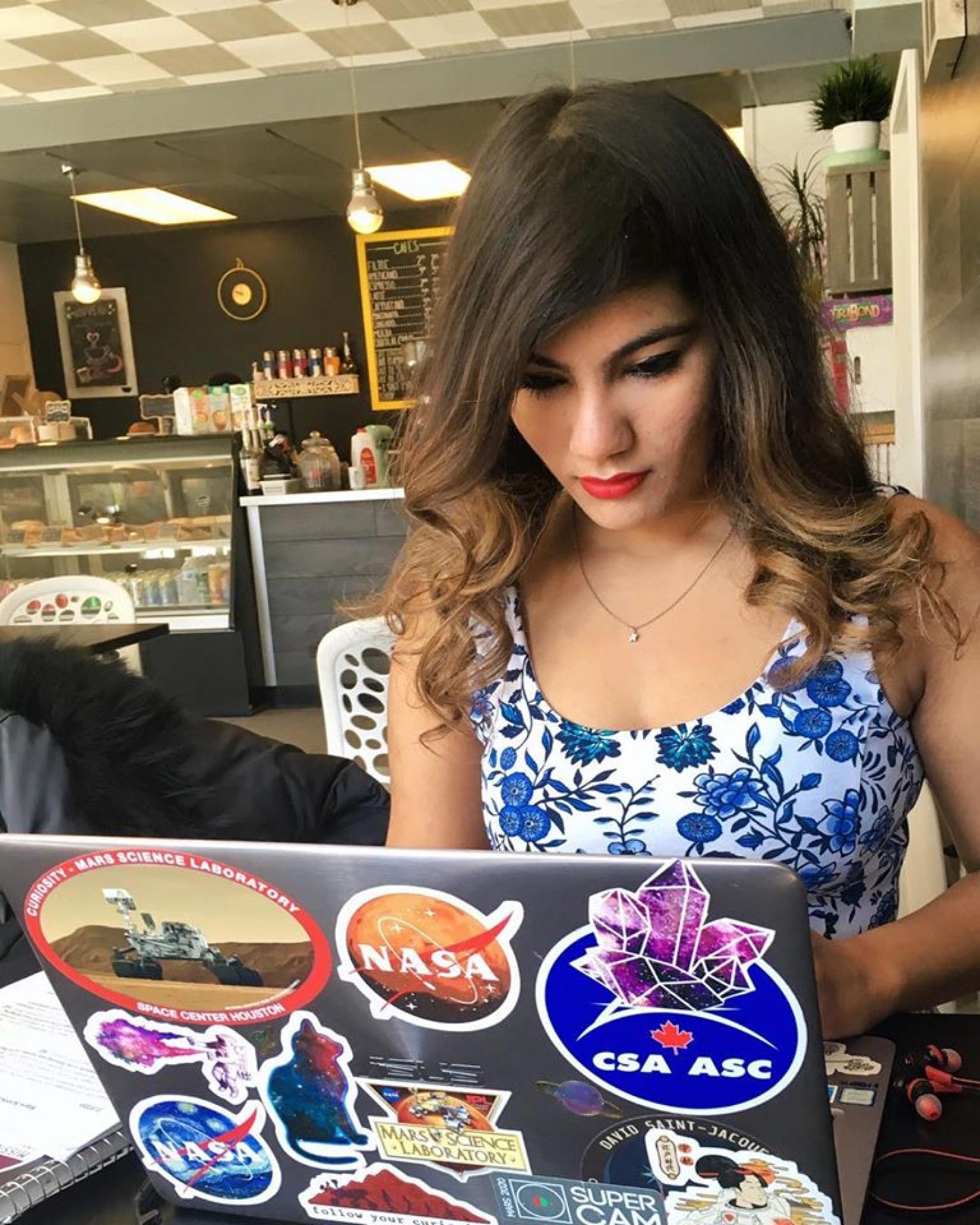 Debarati Das sitting in a cafe with stickers on her laptop